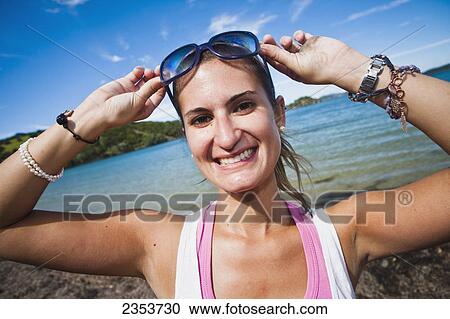 Stock Image - A Young Woman Poses With Sunglasses Along The Coast Of Urupukapuka Island; New Zealand. Fotosearch