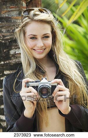 Stock Image - A young woman posing with her camera; Kauai, Hawaii, United States of America. Fotosearch