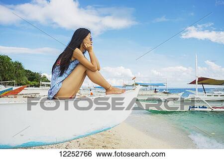Stock Photograph - A young woman resting, watching the seaside on a boat; Bohol, Philippines. Fotosearch
