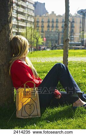 A young woman sits against a tree on the grass with a shopping bag; Barcelona, Spain View Large Photo Image Stock Photography - A young woman sits against a tree on the grass with a shopping bag; Barcelona, Spain. Fotosearch