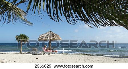 A Young Woman Sits Reading On The Beach; Utila Island, Honduras View Large Photo Image Stock Photo - A Young Woman Sits Reading On The Beach; Utila Island, Honduras. Fotosearch