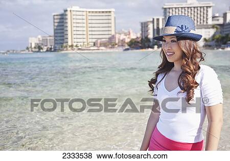 A young woman stands at the water's edge with condominiums along the coast in the background; Honolulu, Oahu, Hawaii, United States of America View Large Photo Image Stock Photo - A young woman stands at the water's edge with condominiums along the coast in the background; Honolulu, Oahu, Hawaii, United States of America. Fotosearch