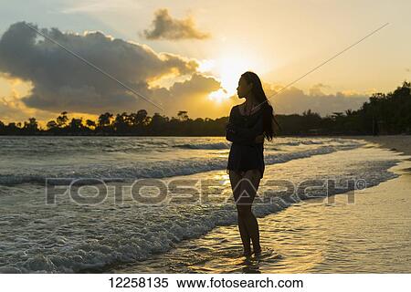 Stock Photography - A young woman stands posing on Sokha Beach at sunset; Sihanoukville, Cambodia. Fotosearch