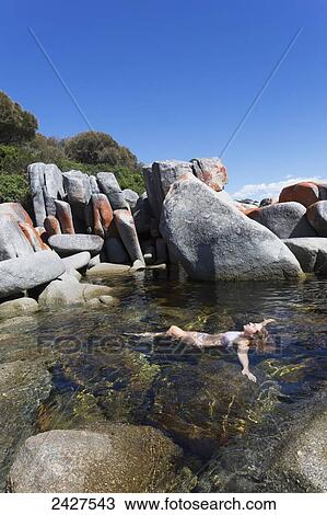 Stock Image - A young woman swims alone among the large rocks off Bay of Fires beach; Tasmania, Australia. Fotosearch