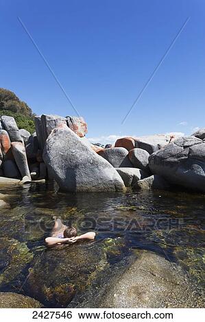 A young woman swims alone among the large rocks off Bay of Fires beach; Tasmania, Australia View Large Photo Image Stock Photograph - A young woman swims alone among the large rocks off Bay of Fires beach; Tasmania, Australia. Fotosearch