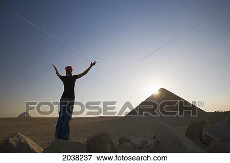 Stock Photo - A Young Woman Tourist Raises Her Arms Toward The Sun And The Red Pyramid; Dashur Egypt. Fotosearch