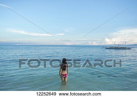 Stock Photo - A young woman wades out in the water off Alona beach; Panglao Island, Bohol, Philippines. Fotosearch