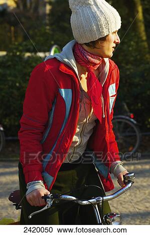 Stock Image - A young woman walking her bicycle; Hamburg, Germany. Fotosearch