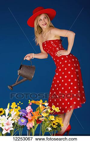 Stock Photo - A young woman wearing red and watering flowers; Edmonton, Alberta, Canada. Fotosearch