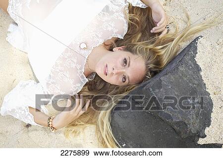 Stock Photo - A young woman with long blond hair and a white sheer top posing on a beach; Maui, Hawaii, United States of America. Fotosearch