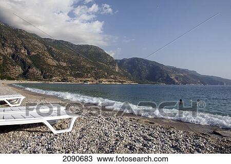 Stock Image - Abandoned Sun Loungers On A Pebbly Beach, The National Park, Oludeniz At The Turquoise Coast, Southern Turkey. Fotosearch