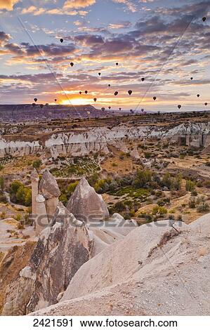 Abundance of hot air balloons flying over the rugged landscape of Honey Valley at sunset; Cappadocia, Turkey View Large Photo Image Stock Image - Abundance of hot air balloons flying over the rugged landscape of Honey Valley at sunset; Cappadocia, Turkey. Fotosearch