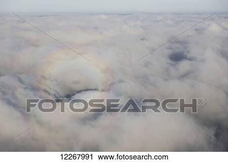 Stock Image - Aerial photo of the sunlight refracting off the water droplets in the air make a glory around a small bush plane shadow visible on the surface of the clouds, Alaska, summer. Fotosearch