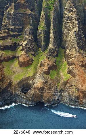 Stock Photo - Aerial view of the rugged coastline and a boat in the pacific ocean along an hawaiian island, Na Pali coast; Kauai, Hawaii, United States of America. Fotosearch