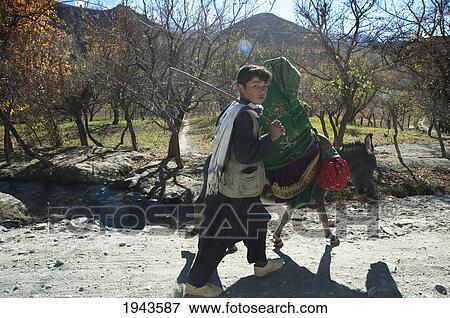 Stock Photo - Afghan Boy Walking Next To A Woman Riding A Donkey Near Shekh Ali, Parwan Province, Afghanistan. Fotosearch