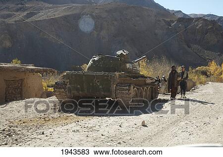 Stock Image - Afghan Men Walk By An Abandoned Soviet Tank In Shekh Ali, Parwan Province, Afghanistan. Fotosearch