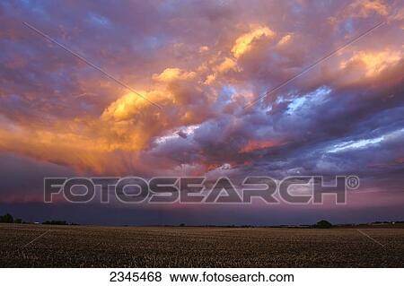Stock Photo - Agriculture - Brilliant clearing clouds pass over a farm field after a Spring storm. The previous year's corn stubble is still present in the field / Central Iowa, USA.. Fotosearch