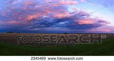 Stock Photo - Agriculture - Brilliant clearing clouds pass over a farm field after a Spring storm. The previous year's corn stubble is still present in the field / Central Iowa, USA.. Fotosearch