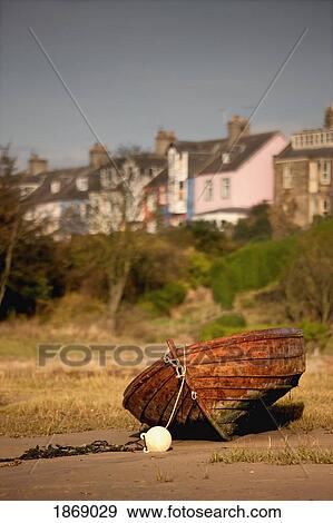Stock Photo - Alnmouth, Northumberland, England; An Abandoned, Rusted Boat Sitting On Land With Houses In The Background. Fotosearch