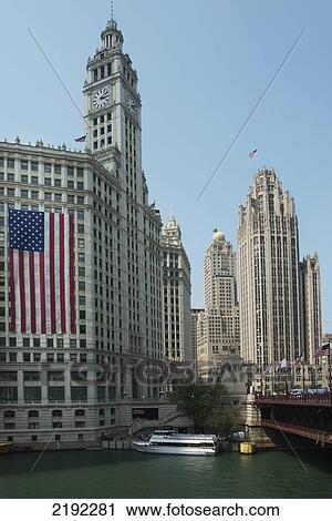 Stock Image - American Flag Hanging On The Side Of A Building With A Clock Tower Along The Chicago River; Chicago Illinois United States Of America. Fotosearch