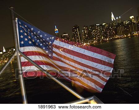 Stock Image - American Flag In Front Of Manhattan Skyline At Night. Fotosearch
