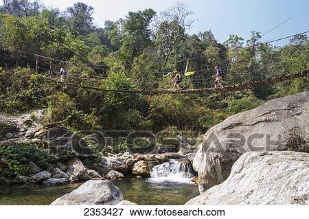 Stock Photo - American Tourists Hike Across A Suspension Bridge Over A Stream On A Trek In Southern Bhutan; Bhutan. Fotosearch