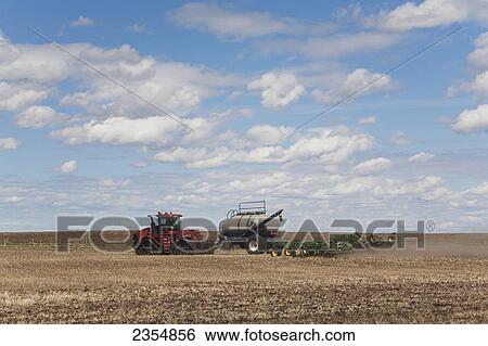 Stock Photograph - An Air Seeder In A Field With A Tractor And Blue Sky With Cloud; Acme, Alberta, Canada. Fotosearch