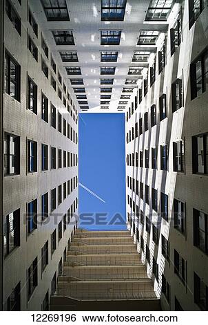 Stock Photograph - An airplane flying in a blue sky and seen from the ground up the walls of a residential building; Denver, Colorado, United States of America. Fotosearch