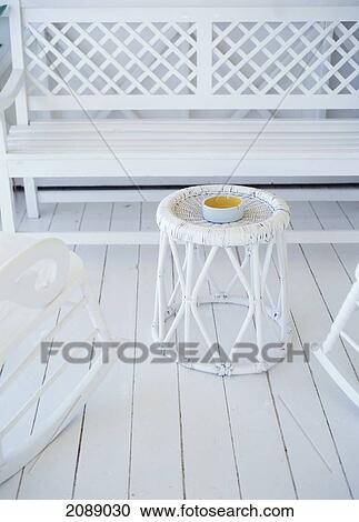 Stock Image - An Ashtray Sits On A White Wicker Table With A White Bench And Rocking Chairs On A White Deck. Fotosearch