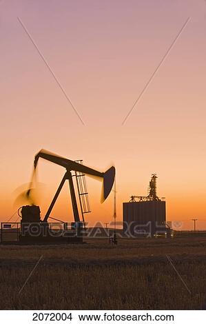 An Oil Pumpjack In Wheat Field With Inland Grain Terminal In The Background, Near Gull Lake, Saskatchewan View Large Photo Image Picture - An Oil Pumpjack In Wheat Field With Inland Grain Terminal In The Background, Near Gull Lake, Saskatchewan. Fotosearch