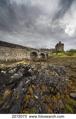 Stock Image - An Old Stone Bridge Leading Towards Old Stone Buildings Under A Cloudy Sky; Kyle Of Lochalsh Scotland. Fotosearch
