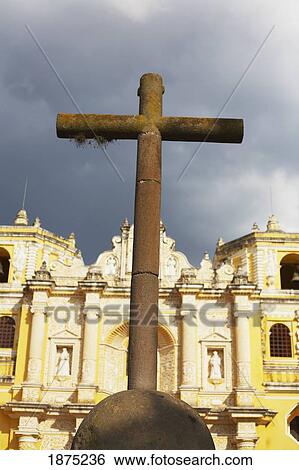 Stock Photograph - Antigua, Guatemala; A Cross In Front Of Buildings And A Cloudy Sky. Fotosearch