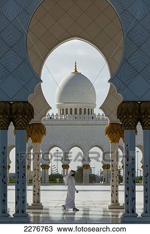 Stock Image - Arab Man Walking Past Courtyard Of The Sheikh Zayed Grand Mosqueabu Dhabi, United Arab Emirates. Fotosearch