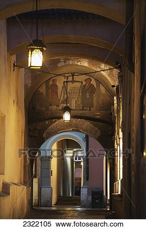 Stock Photography - Arched passageway with fresco and street lamps at night; Bolzano, Alto Adige, Italy. Fotosearch