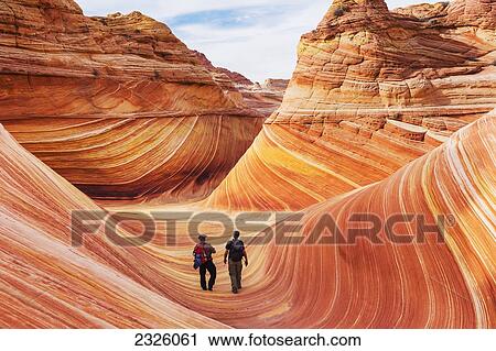 Stock Image - Arizona, Page, North Coyote Buttes, Two Hikers Explore The Rock Formation Called The Wave.. Fotosearch