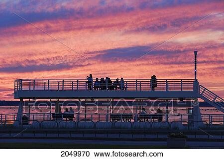 Stock Image - Artist's Choice: People Looking Out At St. Lawrence River And Saint-Barnabe Island At Dusk, Bas-Saint-Laurent Region, Rimouski, Quebec. Fotosearch