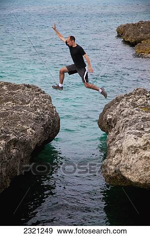 Stock Photo - Aruba, Orangestad, Man jumping rocks on tropical sea. Fotosearch