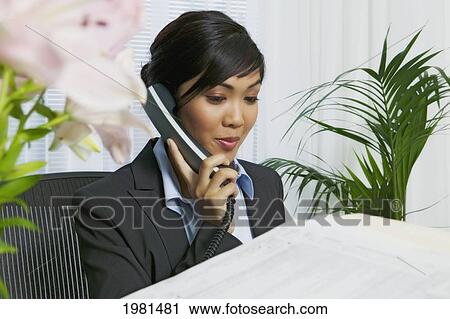 Stock Image - Asian Businesswoman In Office On Phone.. Fotosearch