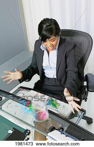 Stock Image - Asian Businesswoman Sitting At Her Office Desk, Paperclips Spilled All Over Her Computer.. Fotosearch