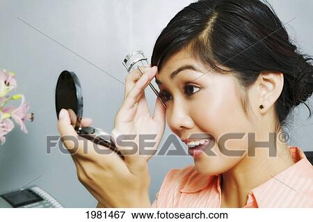 Stock Photo - Asian Businesswoman Sitting At Her Office Desk Putting On Makeup.. Fotosearch