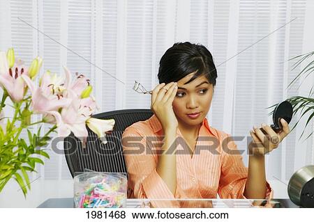 Asian Businesswoman Sitting At Her Office Desk Putting On Makeup. View Large Photo Image Stock Photo - Asian Businesswoman Sitting At Her Office Desk Putting On Makeup.. Fotosearch