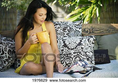 Stock Photo - Attractive Woman Reading In Outdoor Lounge Area With Morning Coffee.. Fotosearch