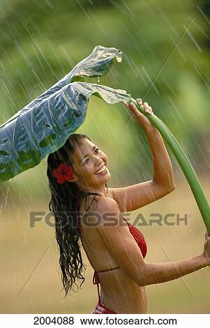 Stock Photo - Attractive Young Woman Using Large Leaf Shade From Rain, Side View, Wearing Red Bikini. Fotosearch
