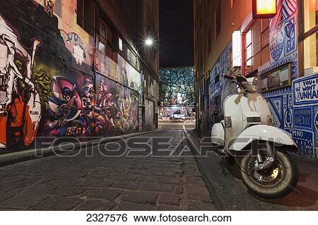 Stock Photograph - Australia, Victoria, View of street Art and moped on Hosier Lane with Federation Square in background; Melbourne. Fotosearch