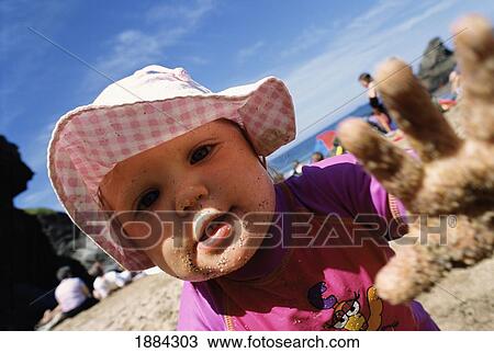 Stock Image - Baby Girl With Sandy Hand On The Beach. Fotosearch