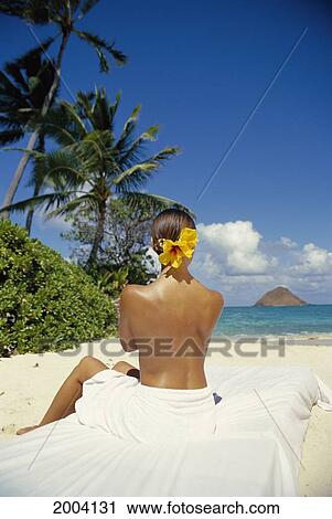 Stock Image - Back View Of Woman Sitting On White Towel At Beach, Looking Toward Ocean, Tropical Setting. Fotosearch