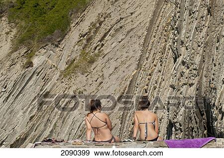 Stock Photo - Back View Of Women Sunbathing In Front Of The Sedimentary Rocks Known As Flysch In Itzurun Beach, Zumaia, Basque Country, Spain. Fotosearch