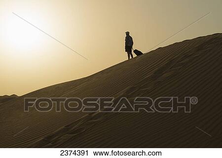 Barefoot man with suitcase on sand dune at dusk; Dubai, United Arab Emirates View Large Photo Image Stock Image - Barefoot man with suitcase on sand dune at dusk; Dubai, United Arab Emirates. Fotosearch