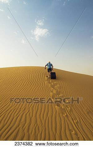 Barefoot man with suitcase walking up sand dune; Dubai, United Arab Emirates View Large Photo Image Stock Image - Barefoot man with suitcase walking up sand dune; Dubai, United Arab Emirates. Fotosearch