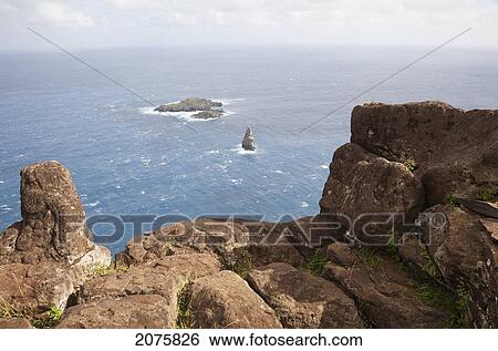 Stock Photograph - Bas Relief Petroglyphs Of Birdman At Mata Ngarau, The Sacred Center Of Orongo. The Islets Of Motu Nui, Motu Iti, And Motu Kao Kao Are Below In The Distance, Rapa Nui (Easter Island), Chile. Fotosearch